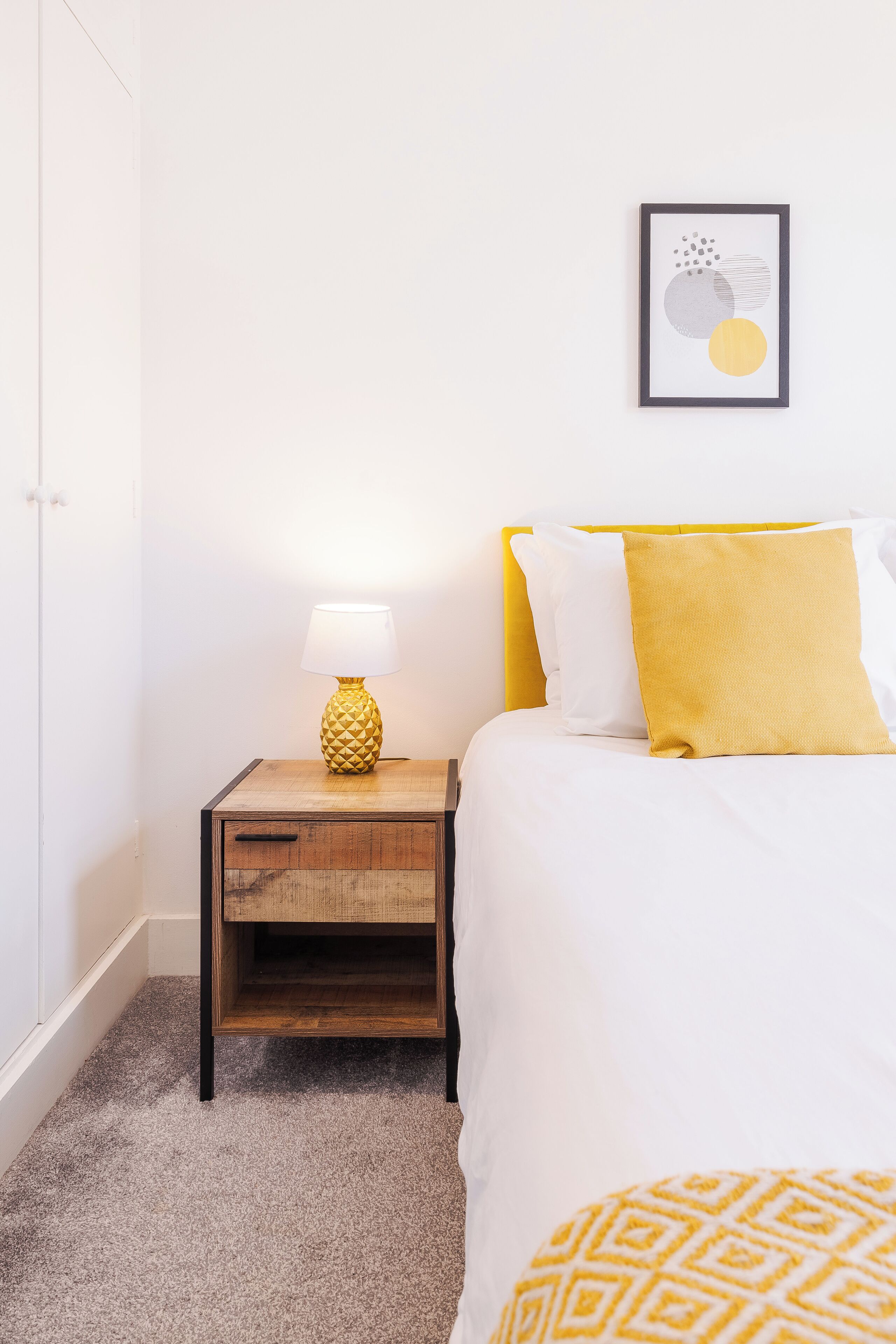 A neatly arranged bedroom with a bed, a nightstand with a lamp, and a framed picture on the wall.