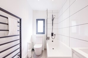 A modern bathroom with a toilet, a bathtub, and a towel rack. - 2 bed flat West Kensington/Fulham (LONDON)