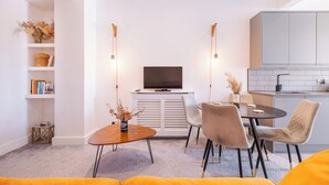 Een moderne woonkamer met een bank, een eettafel met stoelen, een televisie en een keuken met kastjes en een aanrecht.