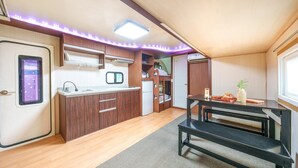Cocina compacta con armarios de madera, un lavamanos, un refrigerador y una mesa de comedor con bancos.