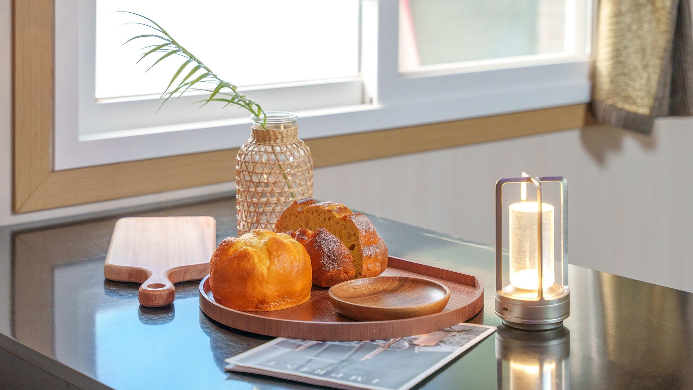 A wooden tray with bread and a candle on a table near a window.