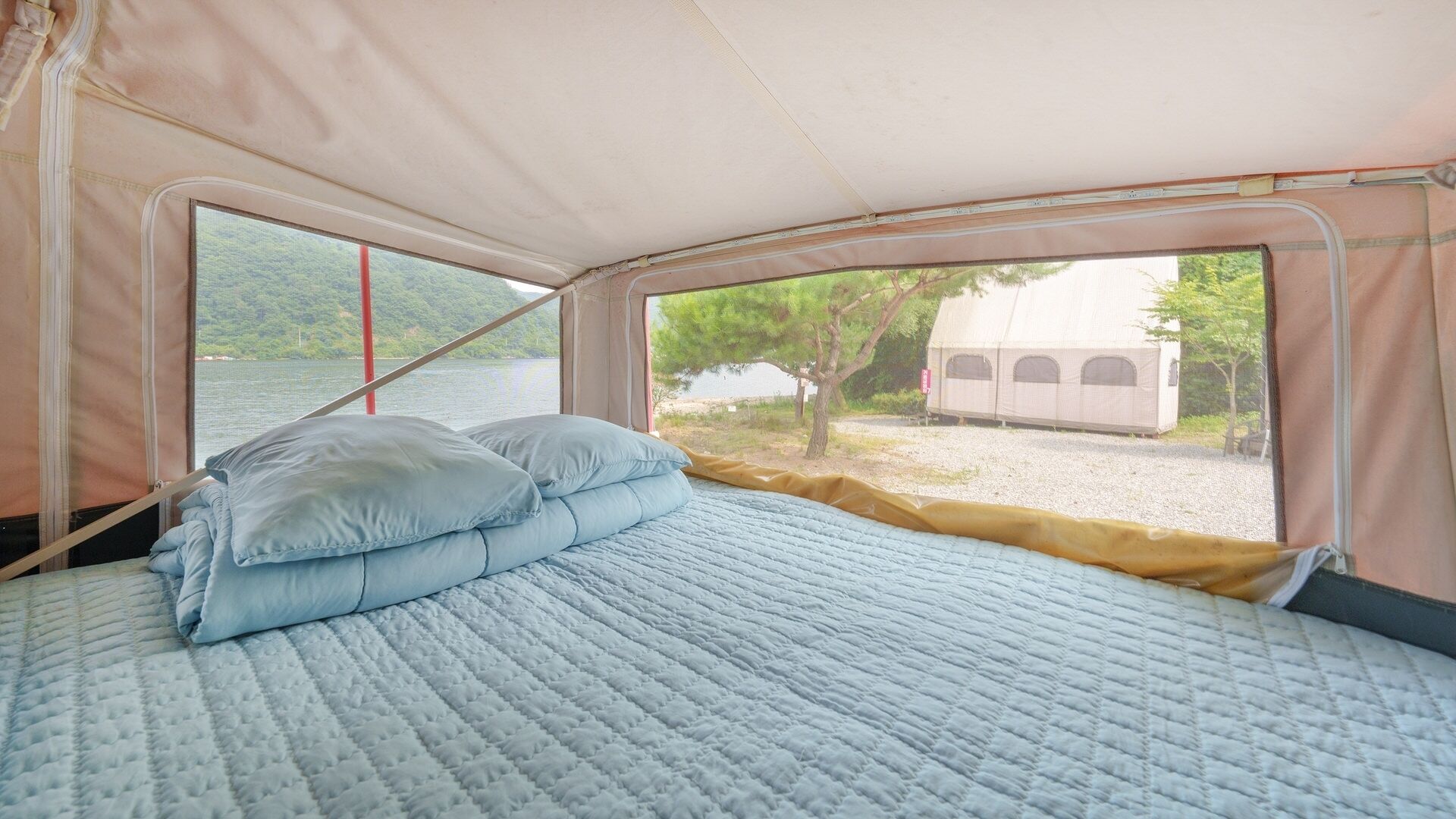 Uma tenda com cama, almofadas e vista para um lago e árvores.
