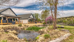 Ein modernes Haus mit einer Veranda, einem kleinen Teich und einem bewaldeten Hintergrund.