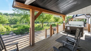 Une terrasse extérieure couverte, dotée d’un jacuzzi, de rampes en bois et offrant une vue sur un paysage naturel.