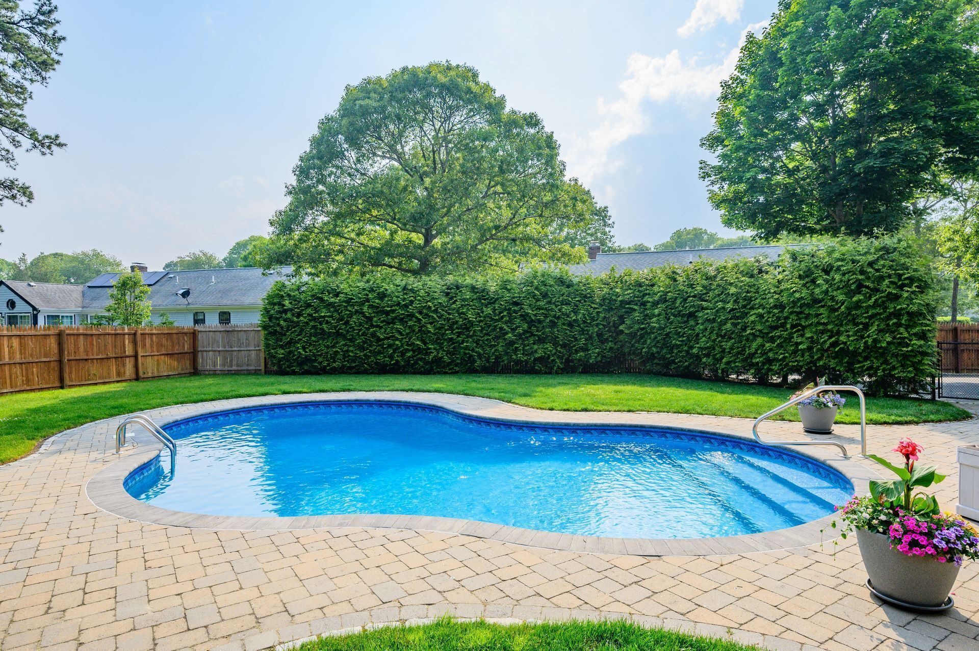 Ein Garten mit Schwimmbecken, Holzzaun und Hecke.