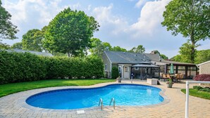 Un patio trasero con piscina, mobiliario de jardín y una zona de estar cubierta.