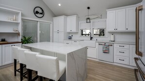 Una cocina moderna con armarios blancos, una isla de mármol y una zona de comedor con sillas blancas.