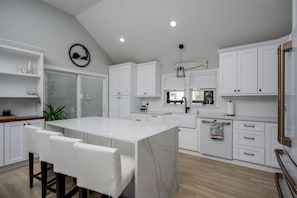 A modern kitchen with white cabinetry, a marble island, and a dining area with white chairs.