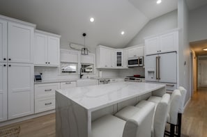 A modern kitchen with white cabinetry, a marble island, and a built-in oven.