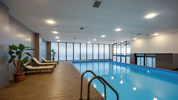Una piscina interior con sillas de descanso, suelo de madera y amplios ventanales.