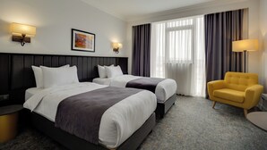 Una habitación de hotel con dos camas, una silla, una lámpara y un cuadro en la pared.