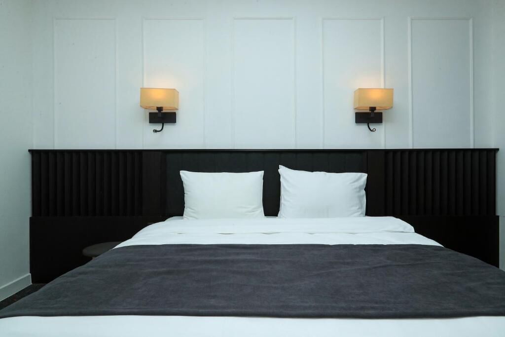 Un lit avec une literie blanche, deux lampes fixées au mur et une tête de lit sombre.
