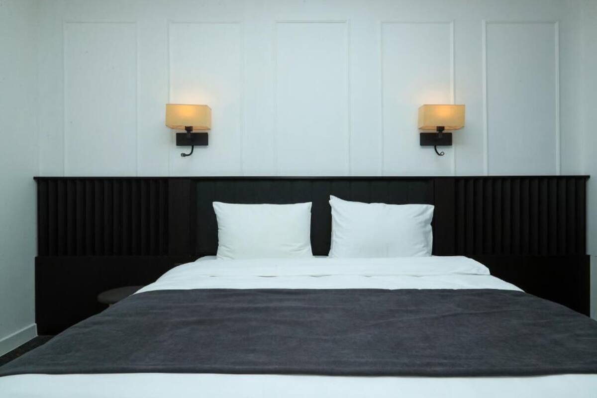 A bed with white bedding, two wall-mounted lamps, and a dark headboard.