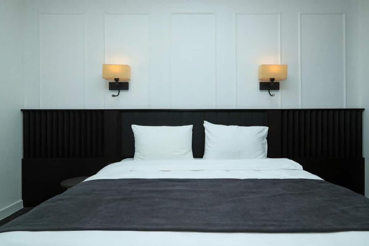 Una cama con ropa blanca, dos lámparas de pared y un cabecero oscuro.