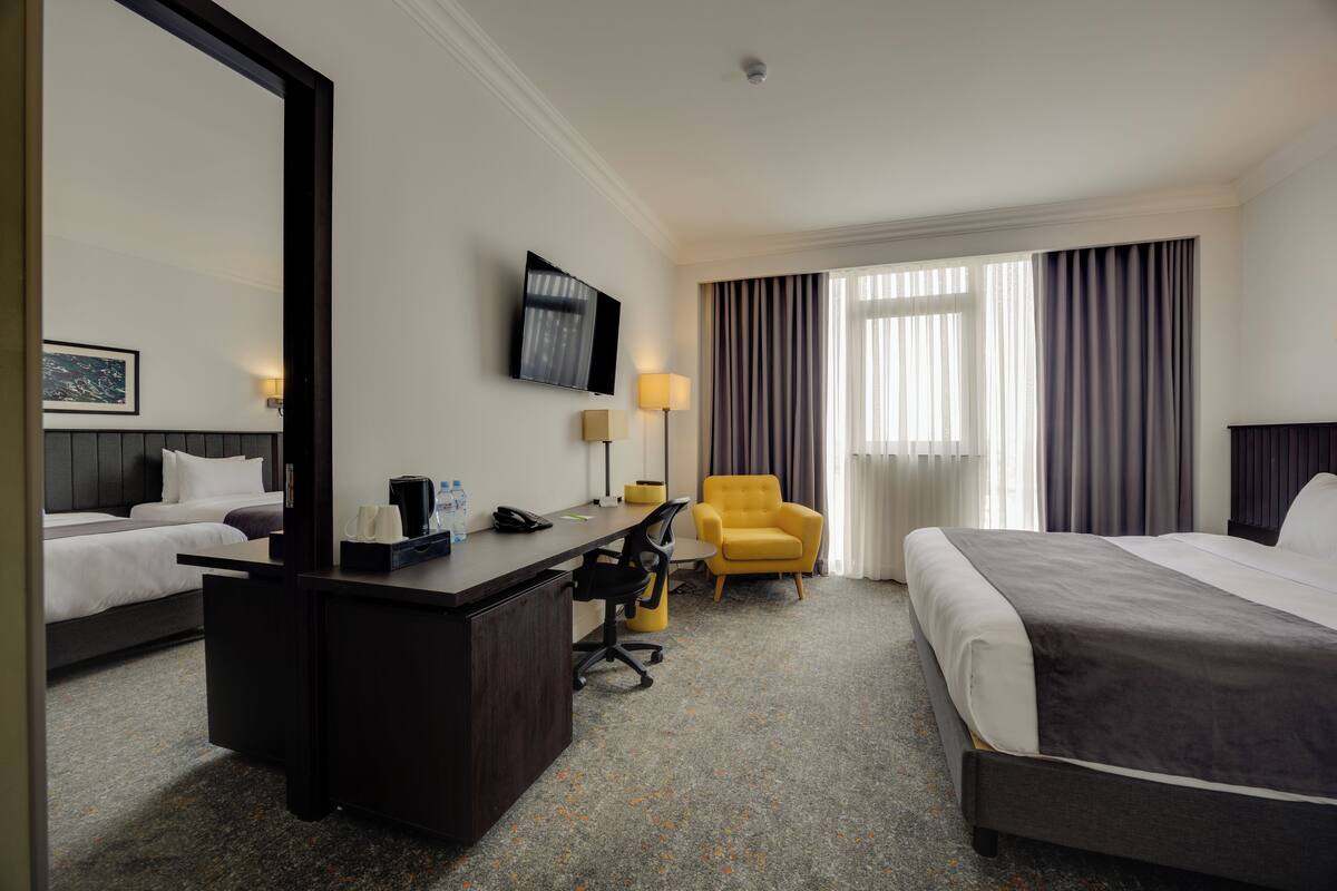 A hotel room with a bed, a desk, a chair, a TV, and a window with curtains.