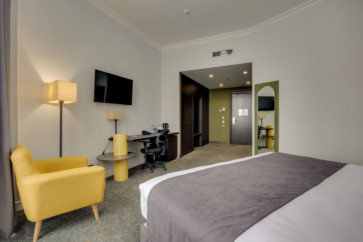 A hotel room with a bed, a desk, a chair, a TV, and a mirror.