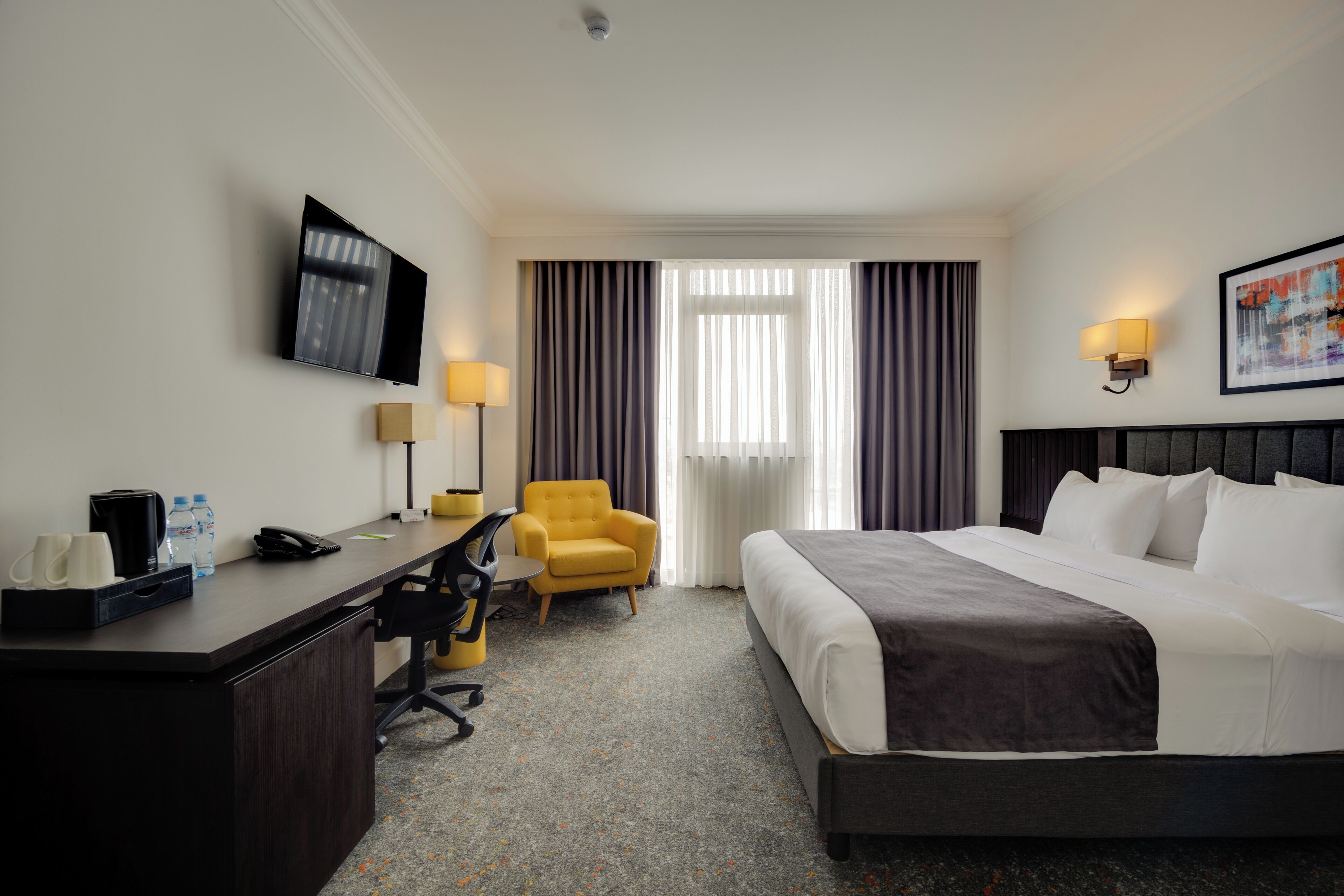 A hotel room with a bed, desk, chair, TV, and curtains.