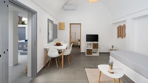 Una habitación moderna y bien iluminada con zona de comedor, sofá, televisor y una pequeña mesa con una planta.
