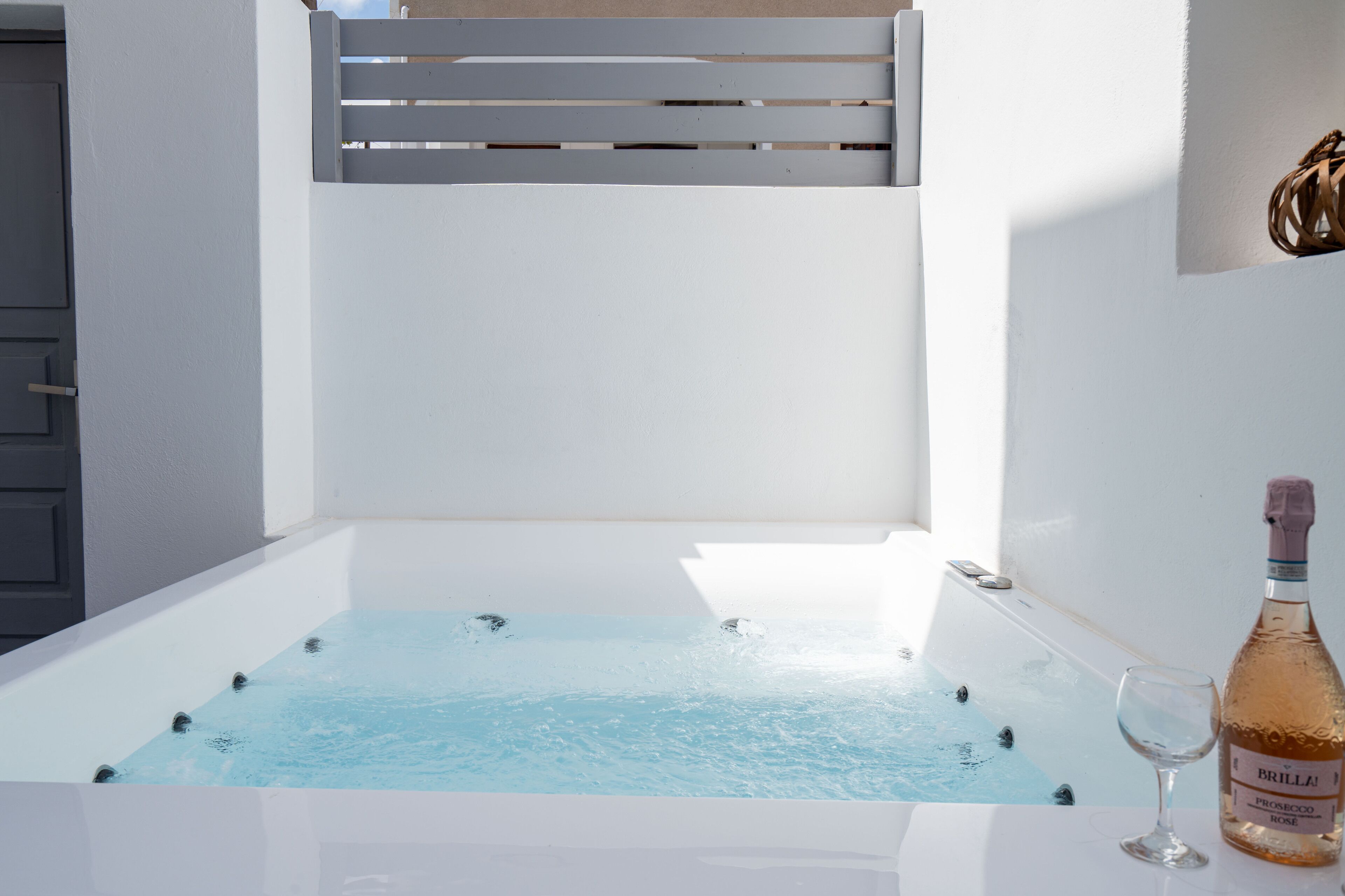 Una bañera de spa con agua, una botella de Brilla Rose y una copa sobre una superficie blanca.