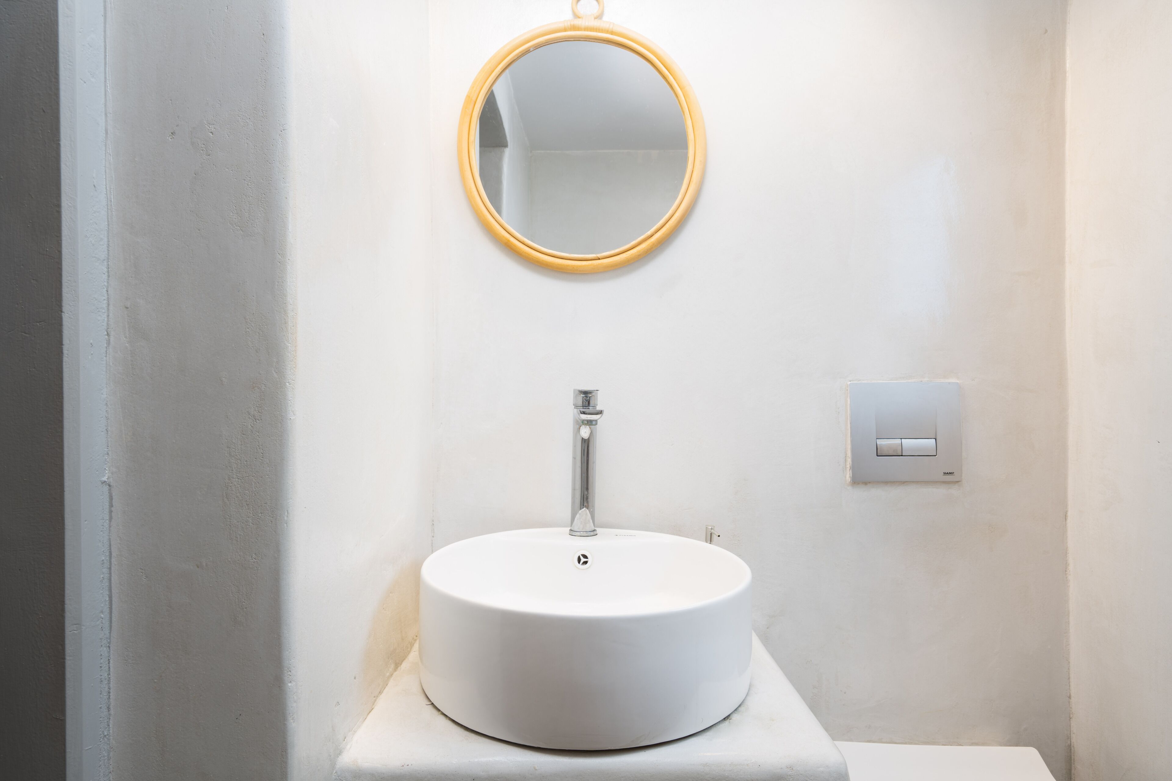 Une salle de bain avec un miroir rond, un lavabo blanc et un interrupteur sur le mur.