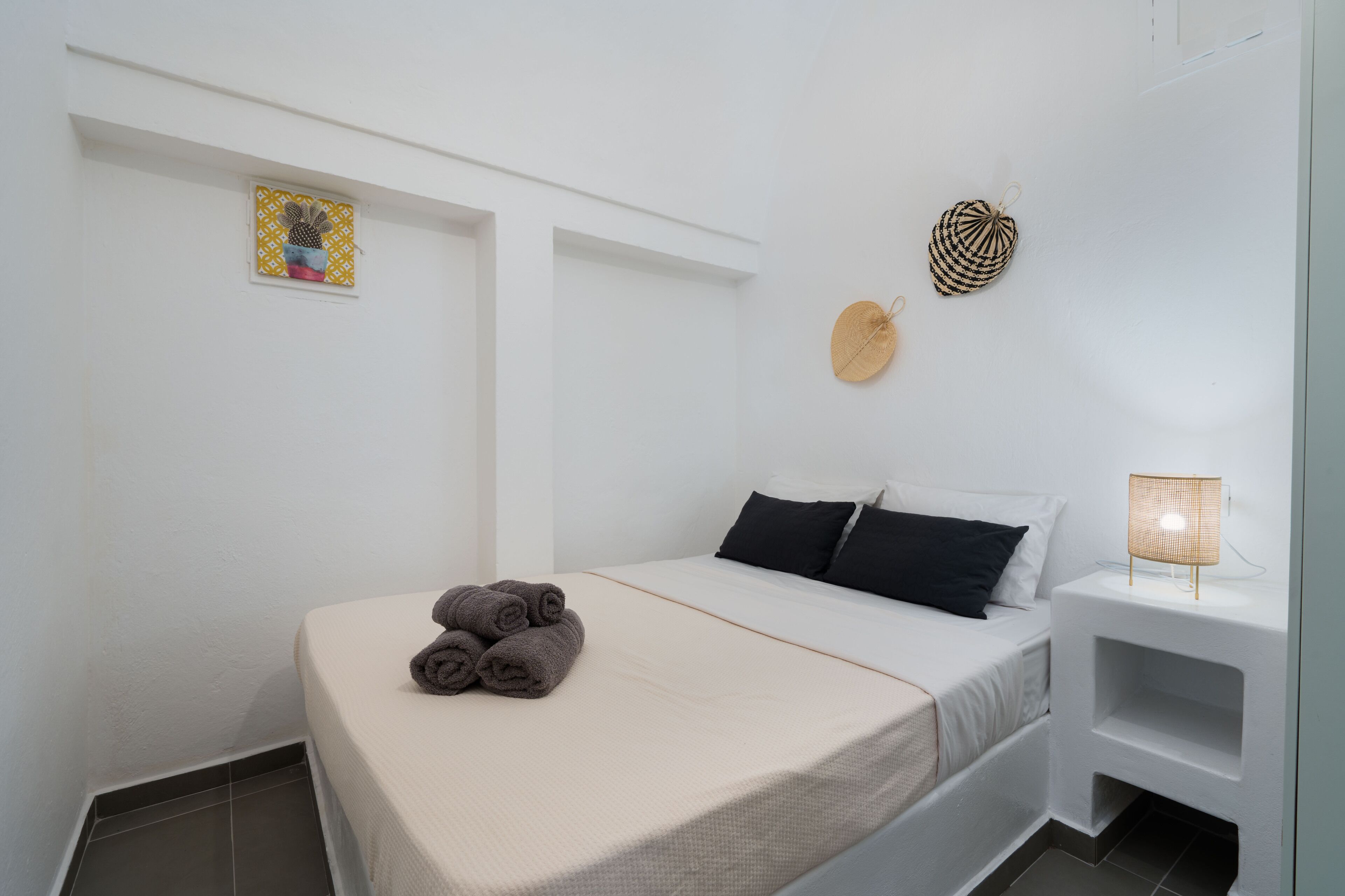 Une chambre d’hôtel minimaliste, avec un lit simple, une petite table de chevet avec une lampe et un élément décoratif fixé au mur.