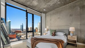 Ein modernes Schlafzimmer mit einem großen Bett, Blick auf die Stadt und einer Wand aus Beton.
