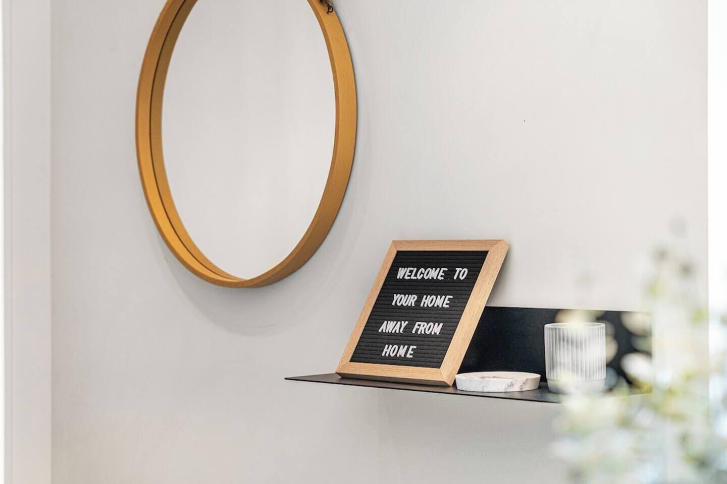 A wall-mounted wooden mirror and a welcome sign on a blackboard.