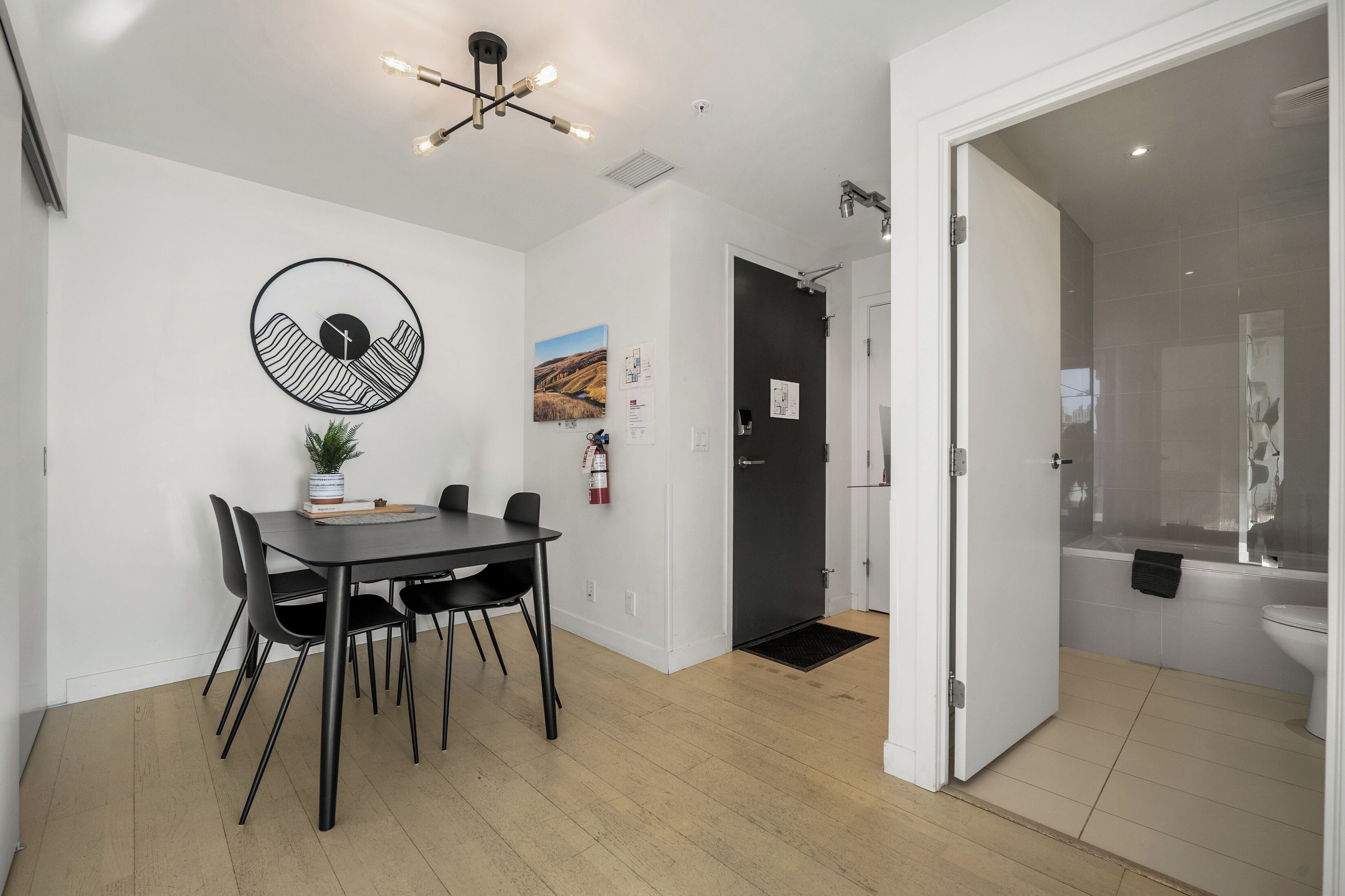 A modern kitchen with a dining table, chairs, a hanging light fixture, and a view into the adjacent bathroom.