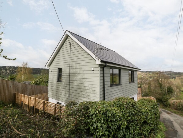 Une petite maison de plain-pied, avec un toit à pignon, une clôture en bois et une haie devant.