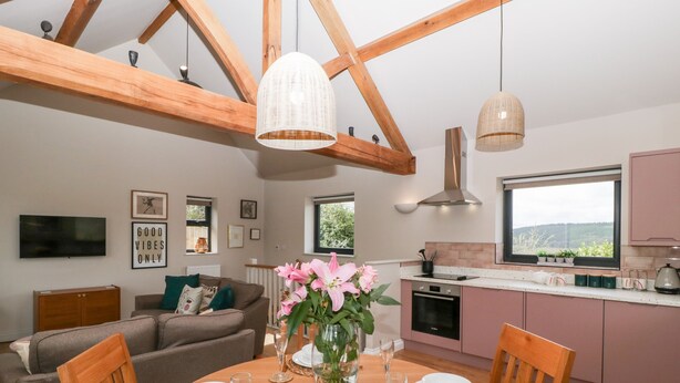 A modern kitchen with wooden beams, a dining table set for six, and a view of the outdoors through a window. - Sevenwoods View (Longhope)