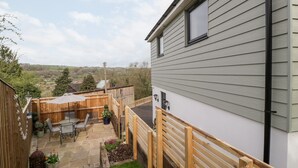 A patio with a table and chairs, a wooden fence, and a view of the countryside. - Sevenwoods View (Longhope)