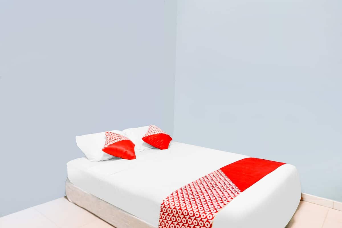 A neatly made bed with white bedding and a red accent, positioned against a light blue wall.