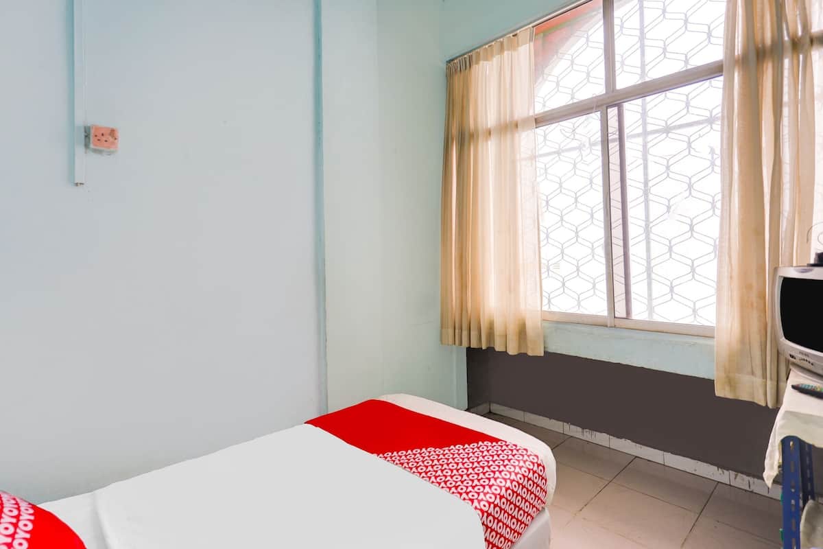 A room with a bed, a window with curtains, a television, and a wall socket.