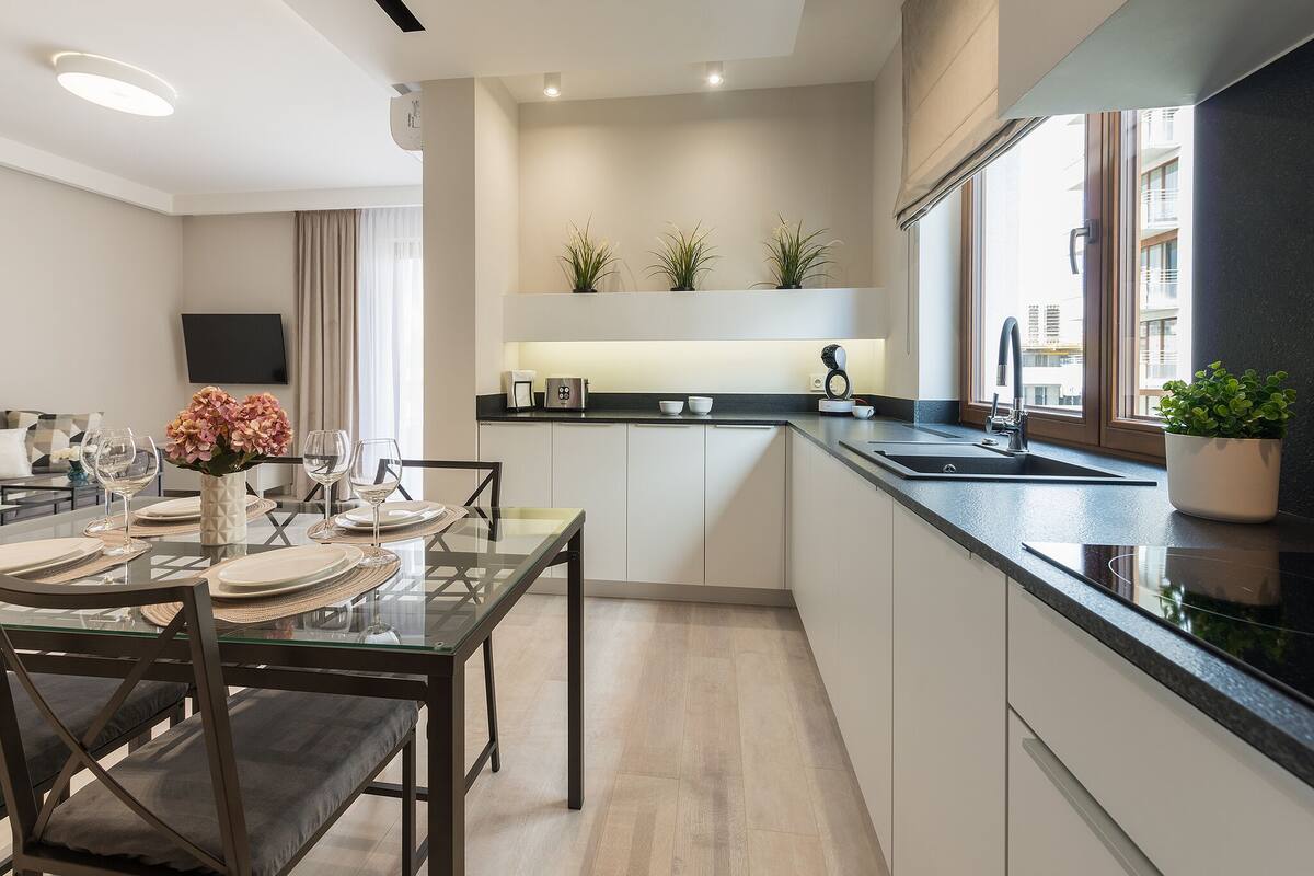 A modern kitchen with a dining area, built-in appliances, and potted plants.