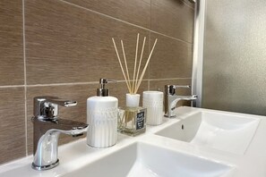 A bathroom with a white sink, two faucets, and a mirror. There are three white containers on the sink, one with a pump dispenser and two with reed diffusers. - Fantastic apartment with a terrace (Milano)