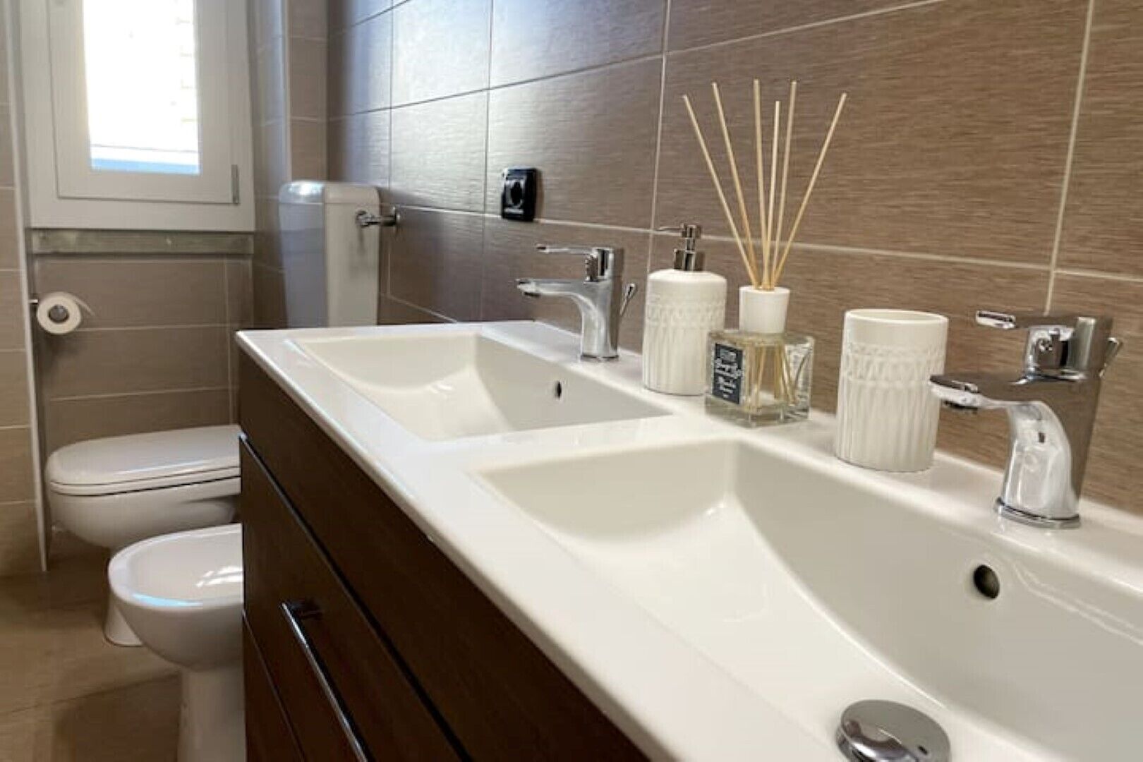 Een moderne badkamer met twee wasbakken, toilet en raam.