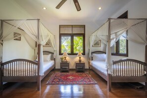 Une chambre à coucher avec deux lits en bois, chacun surmonté d’un baldaquin, un tapis rouge à motifs et deux lampes de chevet.