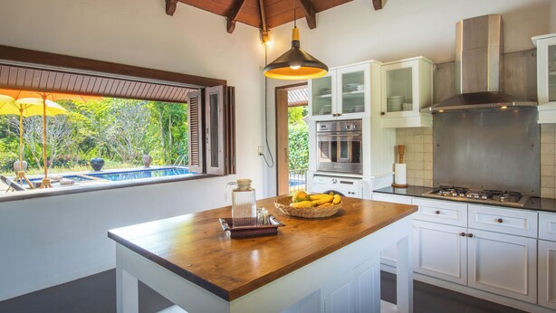 A kitchen with a wooden island, white cabinets, stainless steel appliances, and a view of a swimming pool.