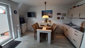 A compact kitchen with a dining table, chairs, a TV, and a lamp.