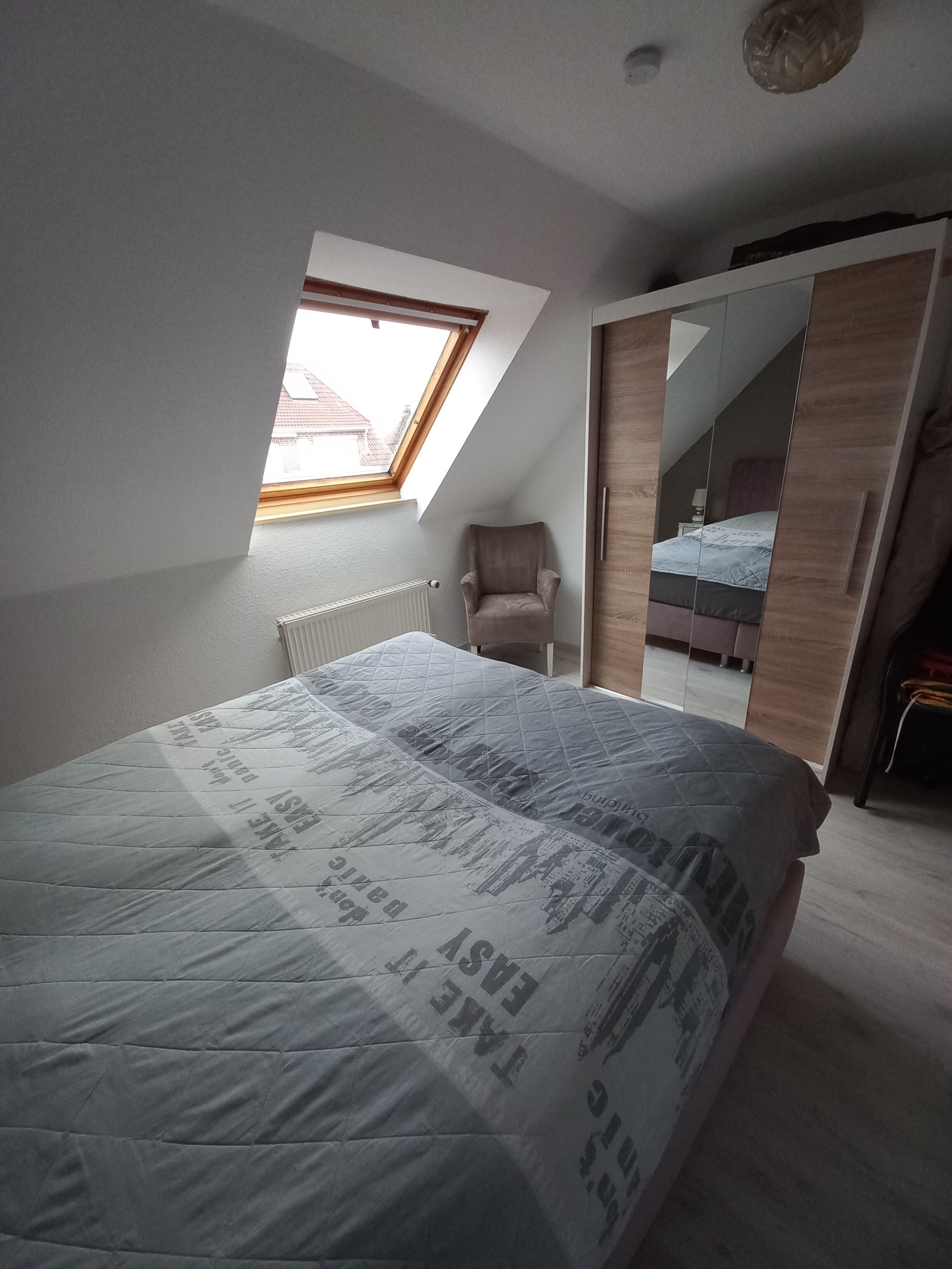 A bedroom with a bed, a window, a chair, and a mirror.