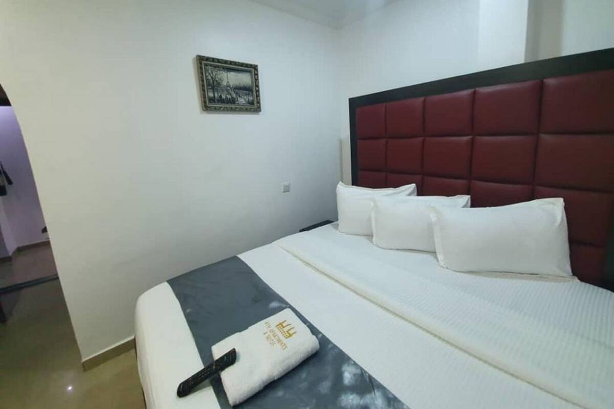 A hotel room with a bed, a headboard, a pillow, a remote control, and a wall-mounted picture.