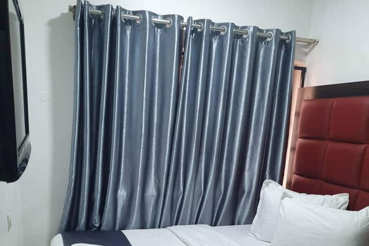 A hotel room with a bed, a telephone on a wooden table, and a curtain.