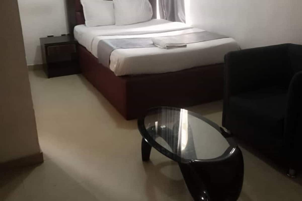 A hotel room with a bed, a glass coffee table, a sofa, a nightstand, and a painting on the wall.