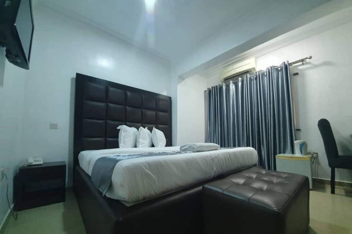 A bedroom with a bed, a small table, a chair, and a window with curtains.
