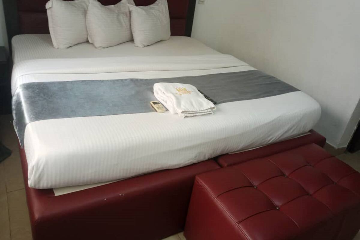 A bed with white bedding, a grey blanket, and a red upholstered bench.