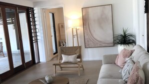 Una sala de estar con un sofá, una silla de madera, una mesa de centro y un cuadro abstracto grande en la pared.