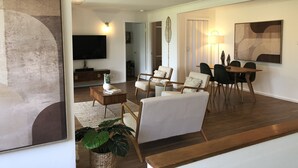Una sala de estar moderna con televisor de pantalla plana, una mesa de centro de madera y un comedor con mesa y sillas de madera.