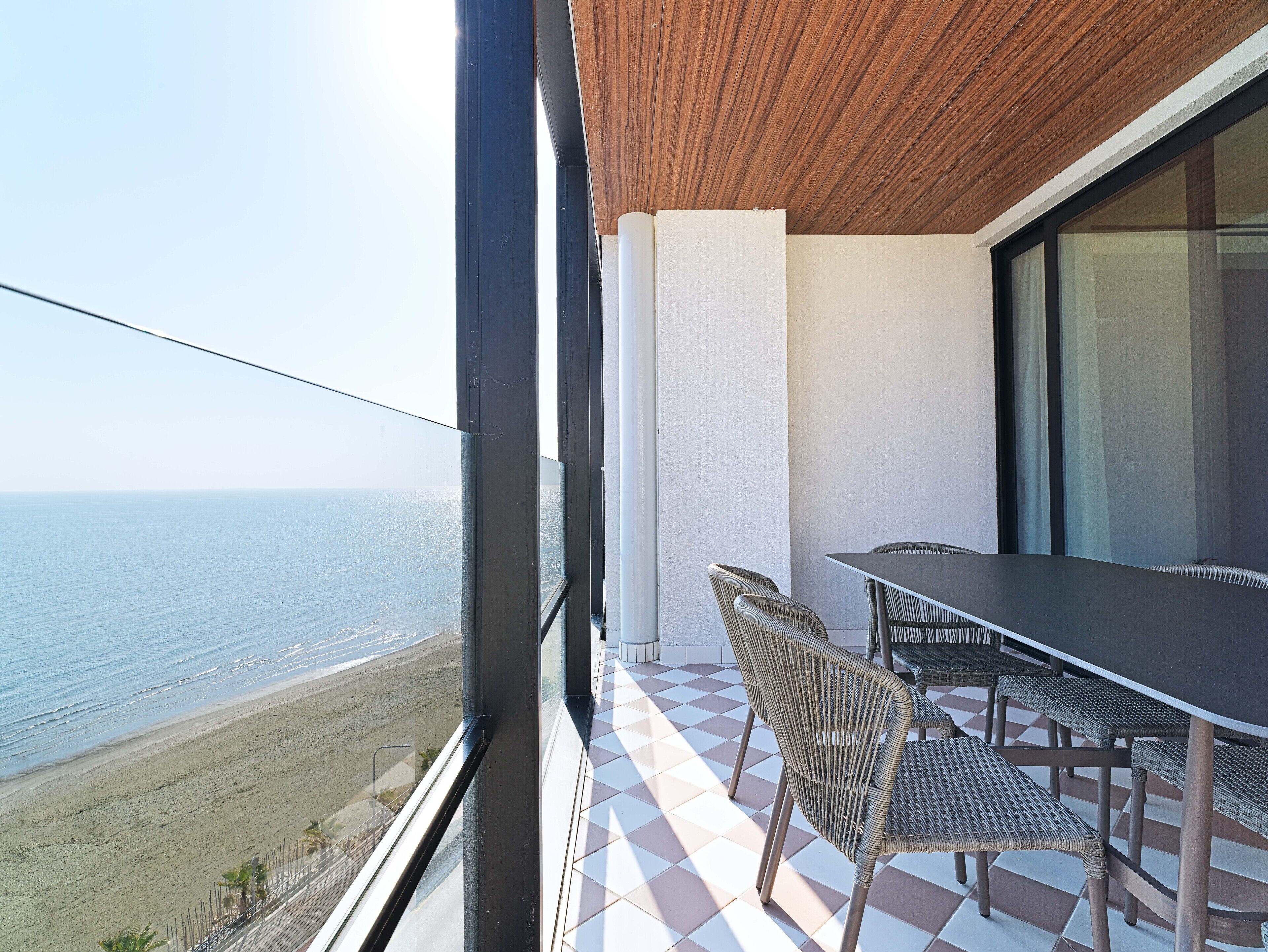 Un balcon avec vue sur la mer, une table et des chaises en osier.