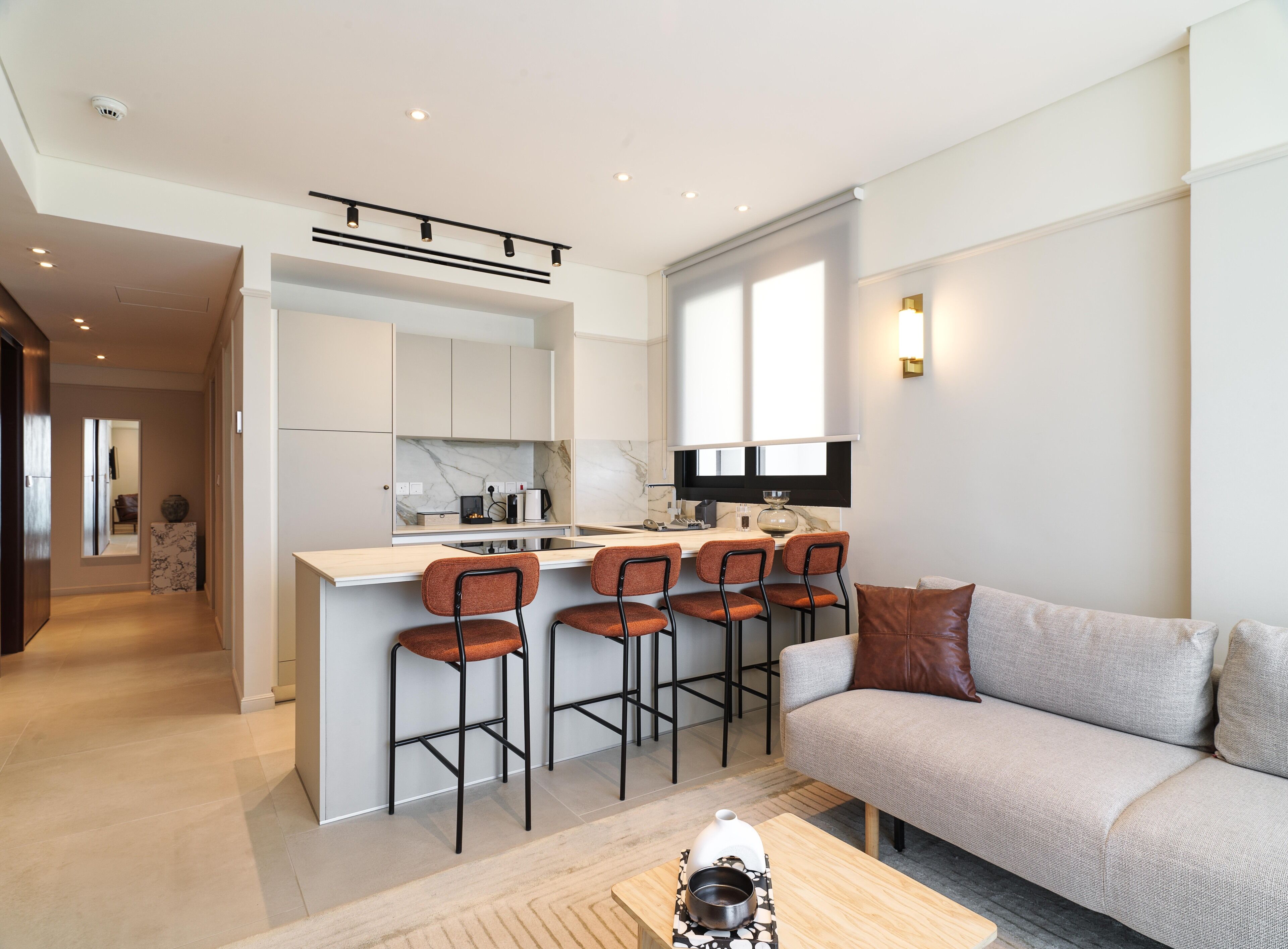 A modern kitchen with a central island, bar stools, and a sofa in a living area.