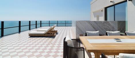 Una terraza moderna al aire libre con suelo a cuadros, sillones de descanso, una mesa de madera y vistas al mar.